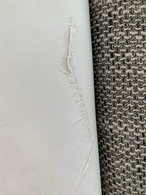 Aus der Polsterwerkstatt Egora: Aufgerissene Stelle im Leder, die den Blick auf das Trägergewebe freigibt (Ecksofa mit Ledersockel, Sofa neu beziehen)