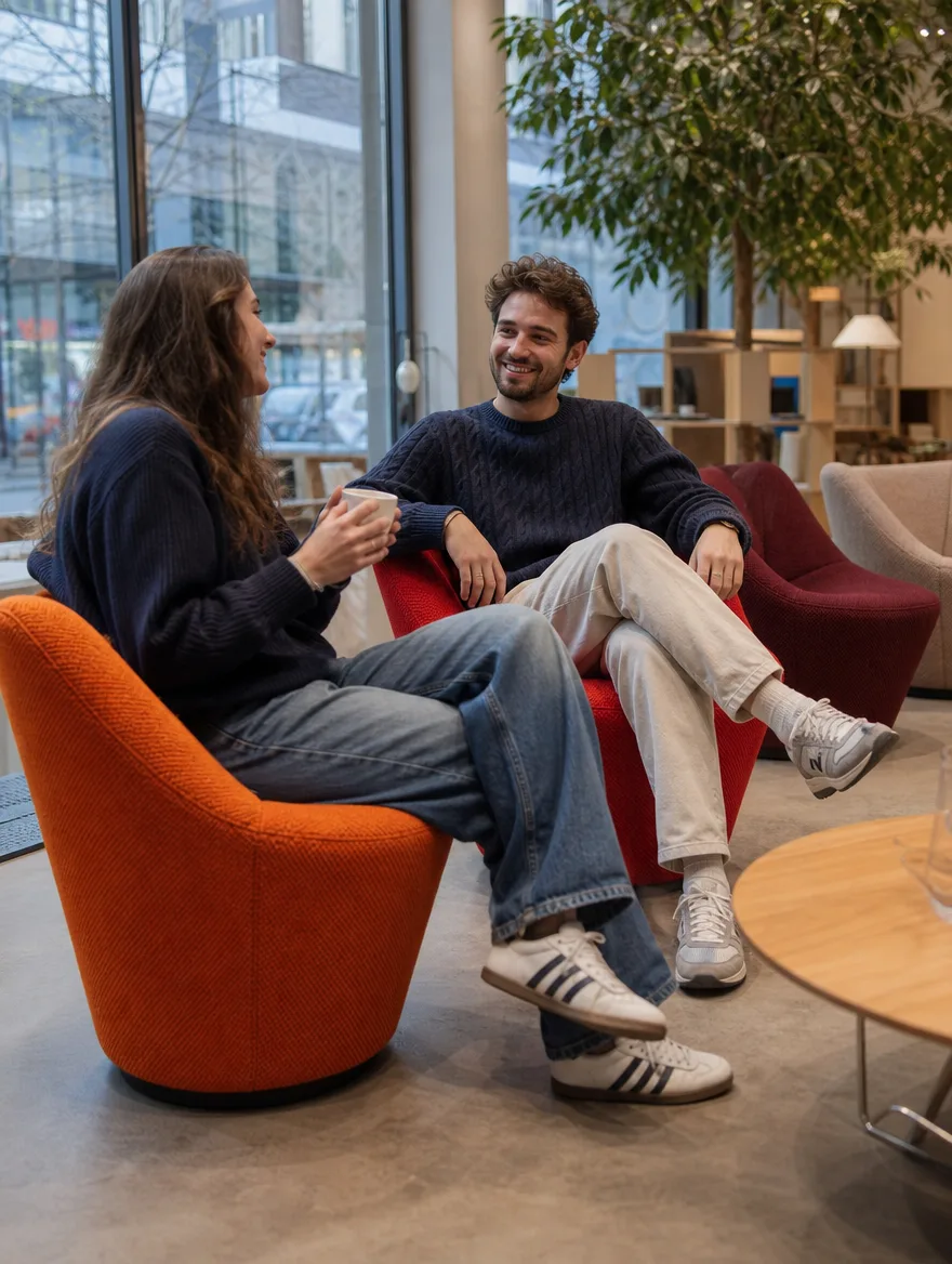 Drehbare Loungesessel in Orange- und Rottönen in der Lounge eines Design-Showrooms, zwei Freunde lachen: Moderne Polsterei